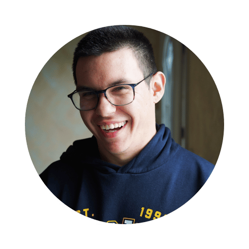 Un jeune homme souriant portant un sweat à capuche dans un environnement intérieur.