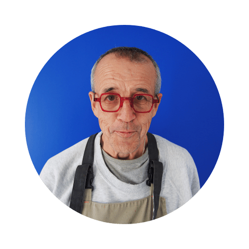 Portrait d'un homme âgé portant des lunettes rouges et un tablier sur fond bleu.